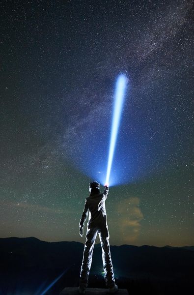 cosmonaut shining flashlight into magnificent night sky